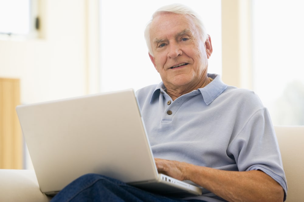 Senior man sitting on couch with laptop, smiling