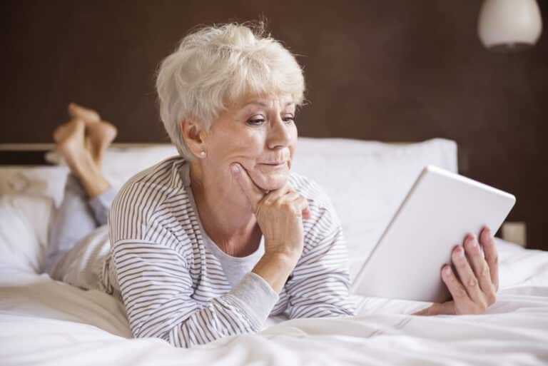 Senior woman looking thoughtfully at tablet in bed