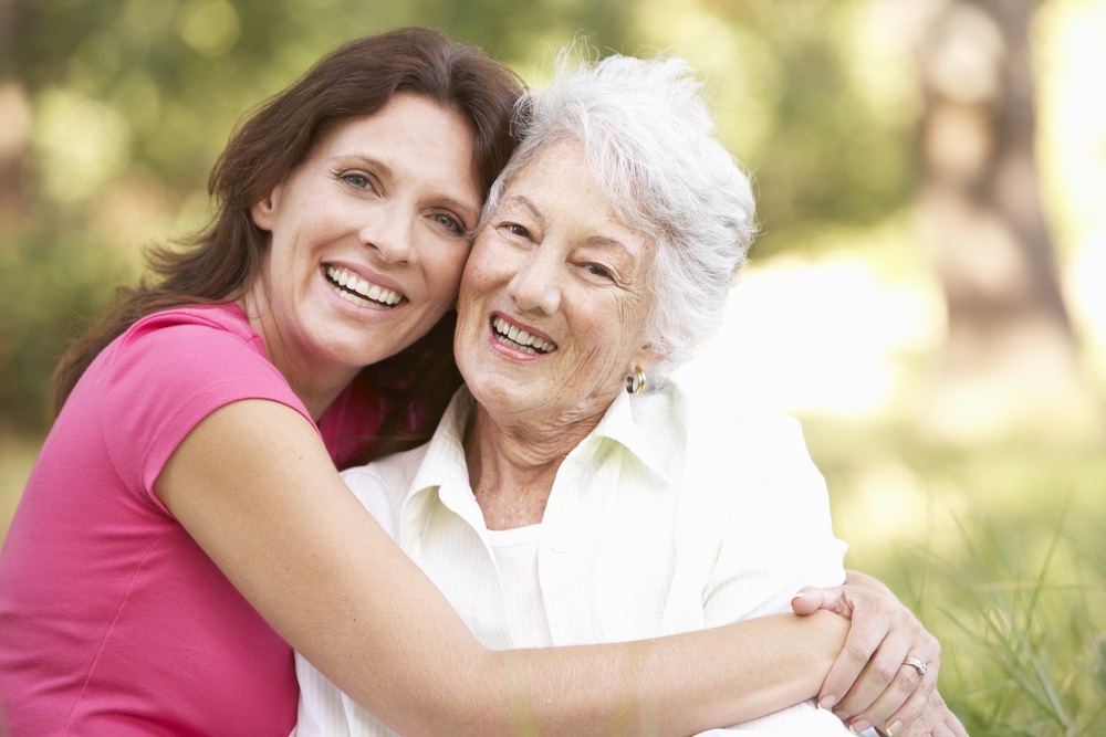 Senior woman and younger woman smiling and hugging outside