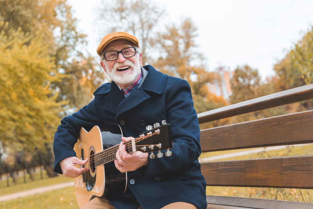 Smiling senior man playing guitar on park bench