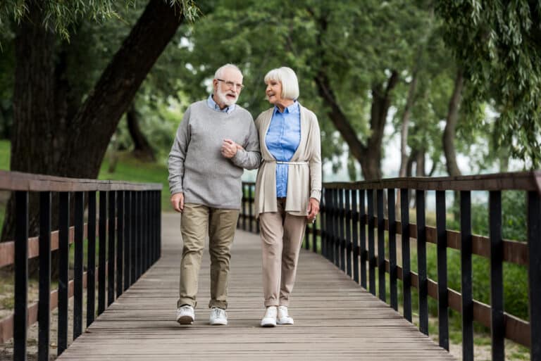 senior couple walking on wooden bridge in park