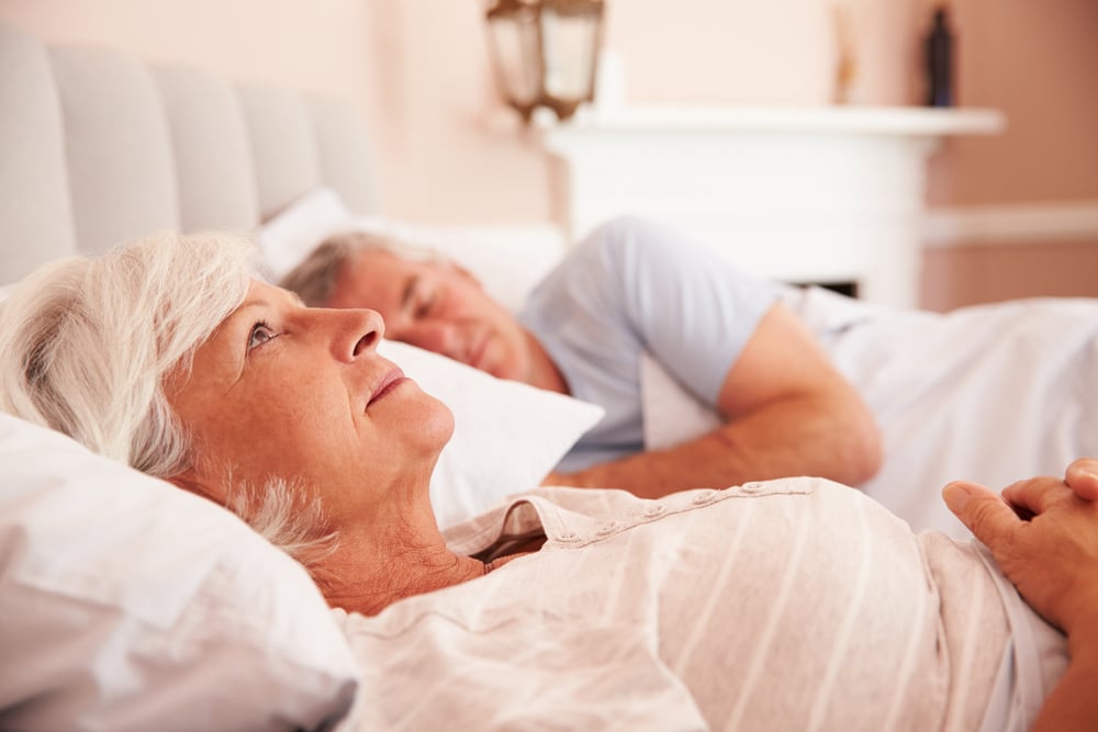 Senior couple in bed, woman staring at the ceiling while man sleeps