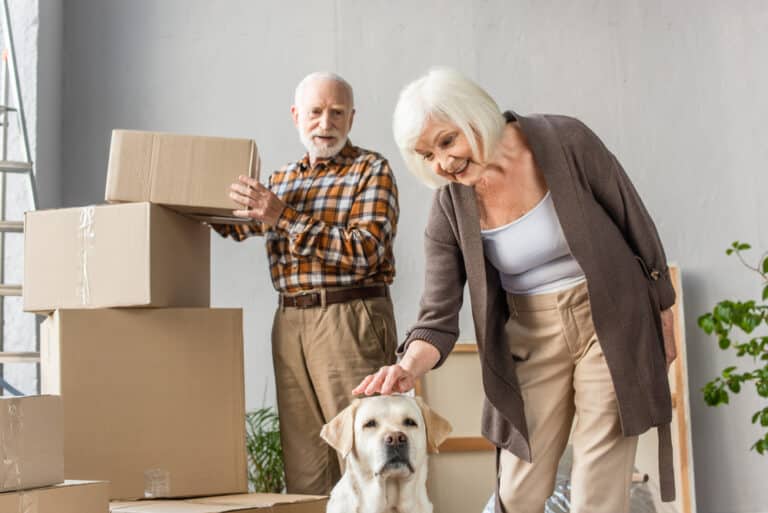 Two seniors with moving boxes and dog, smiling