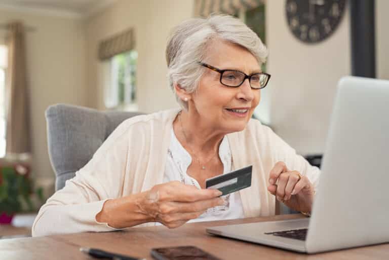 Smiling senior woman paying for something online, using laptop and credit card