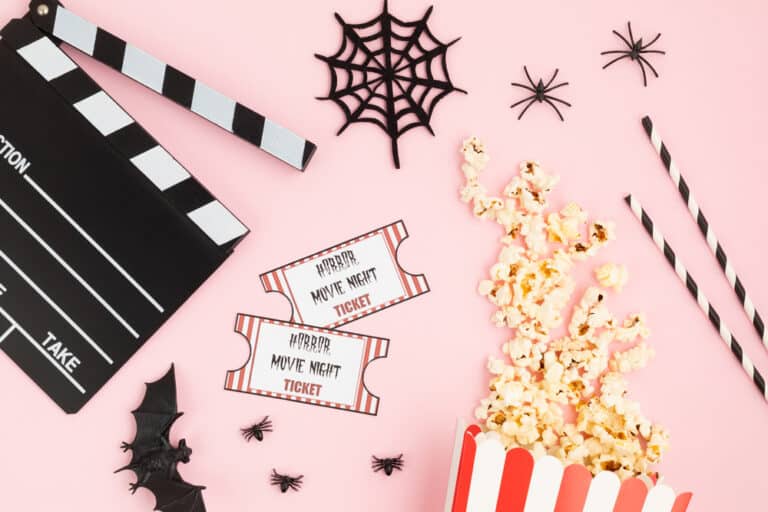 Movie tickets, popcorn, clapperboard, fake spiders, webs, bats on pink background