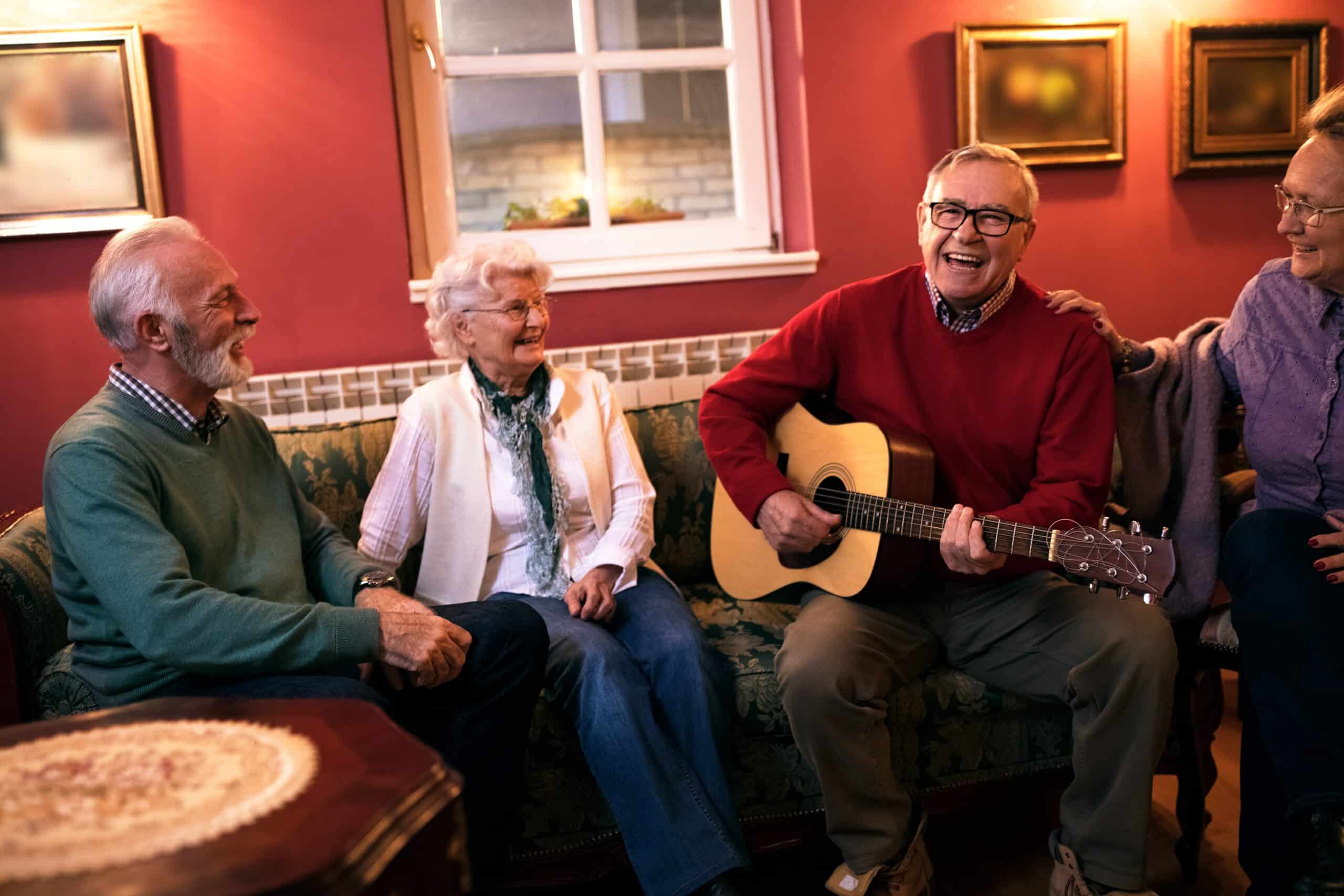 Group of four seniors sitting, one playing guitar