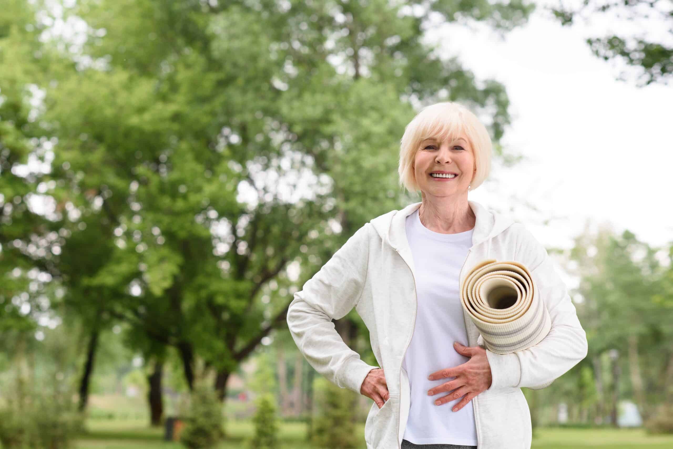 Smiling senior woman holding a yoga mat in the park
