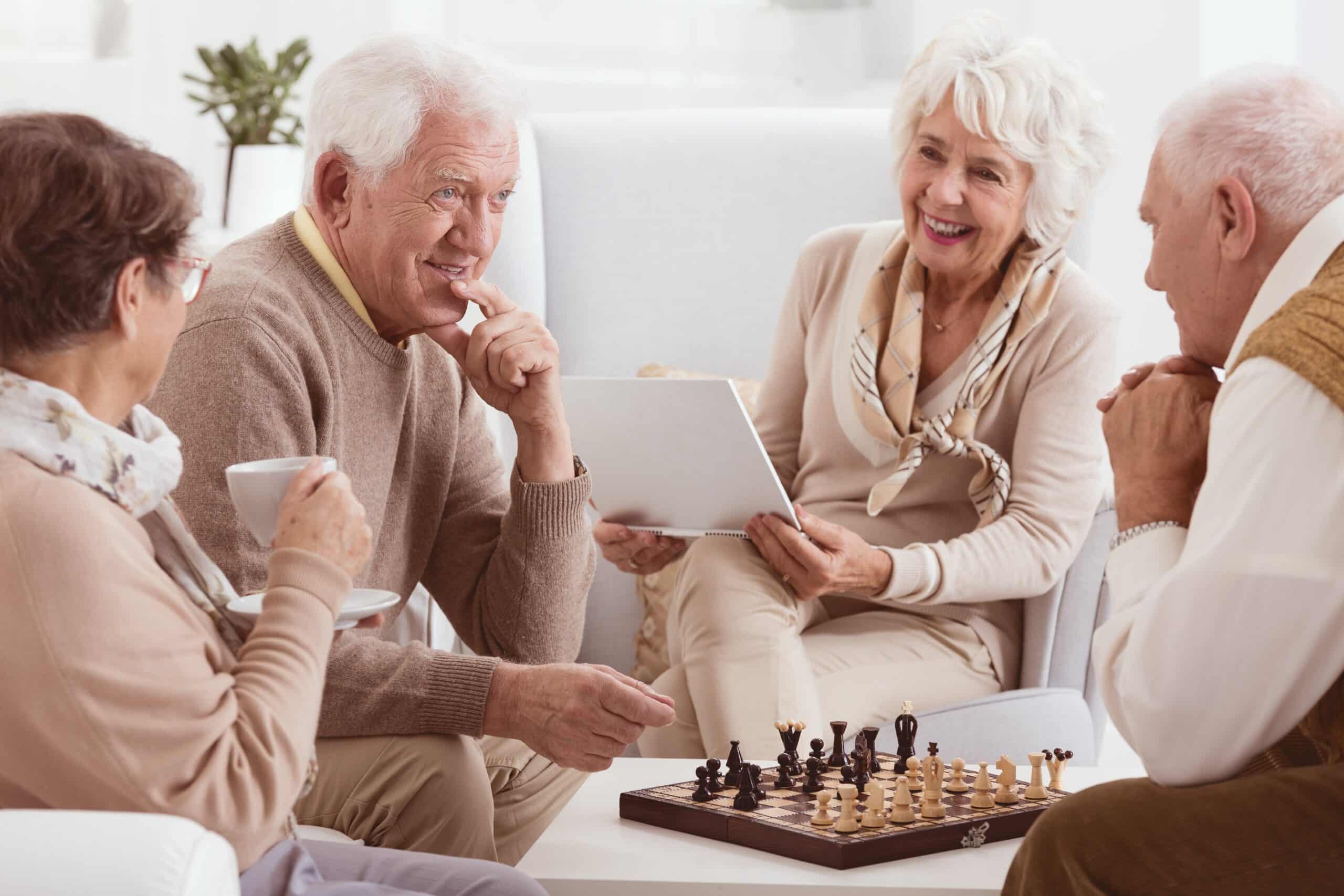 Four seniors socializing happily, playing chess, drinking coffee