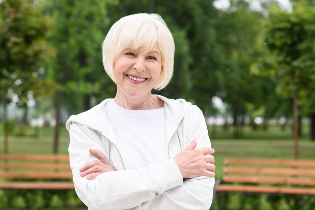 Smiling senior woman standing outside with arms crossed