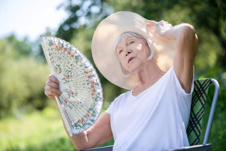 Senior woman outside in summer, wearing sunhat, using fan